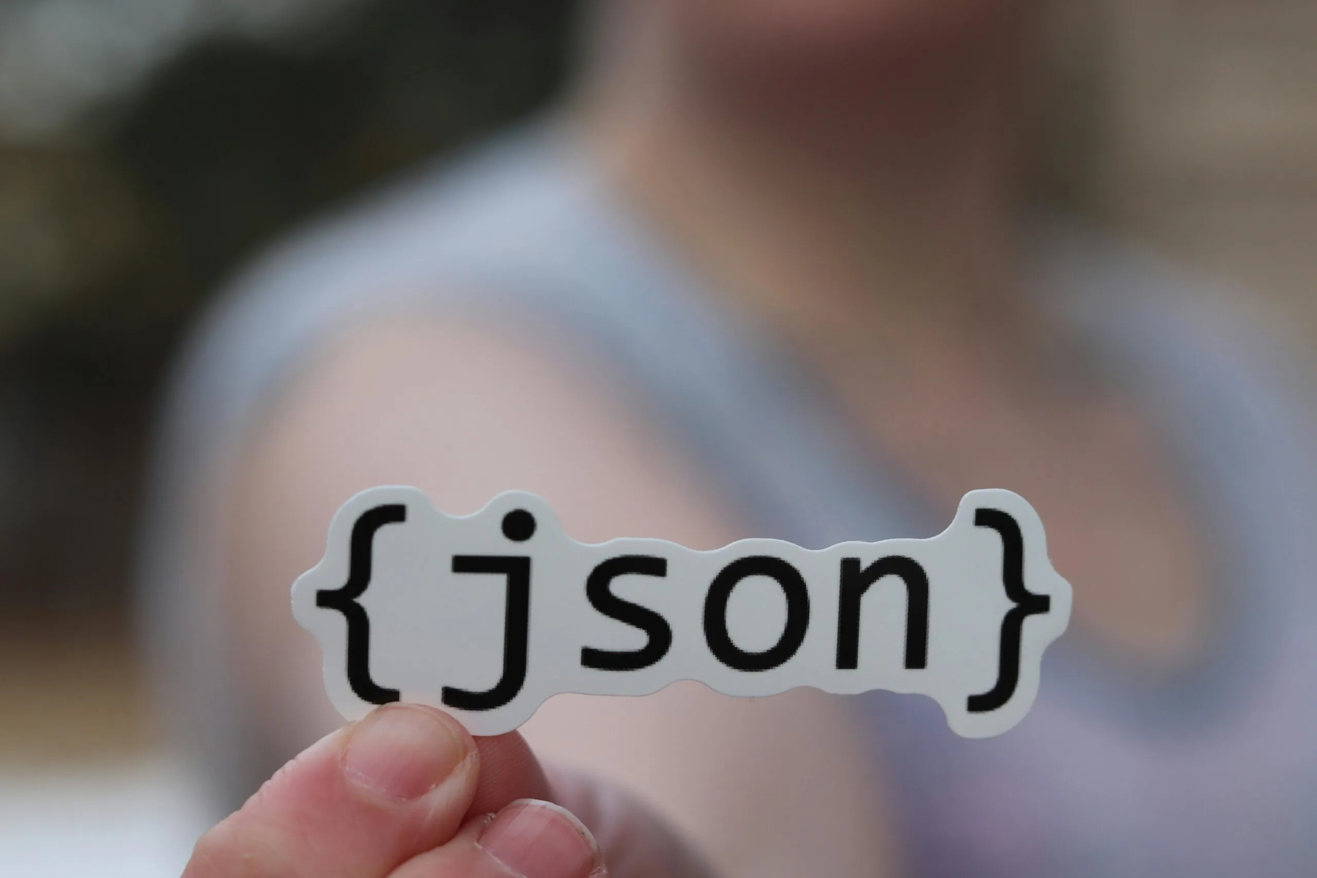 A hand holding a JSON text sticker, symbolic for software development